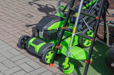 Yeni güçlü yeşil çim biçme makinesi, budayıcı ve satılık merdiven. Bahçe aletlerinin bir çeşidi. Açık havada. Gündüz.