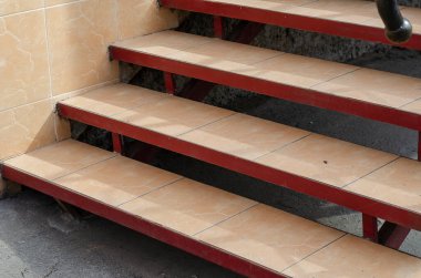 Parmaklıklı kahverengi ve kırmızı basamaklar. Seramik fayanslarla kaplı binaya giriş. Doğal ışık, gündüz. Seçici odak.