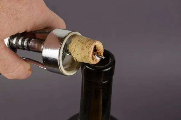 Wine bottle, hand with a corkscrew and a broken cork on a gray background. A man\'s hand holds a corkscrew with a broken wine stopper.