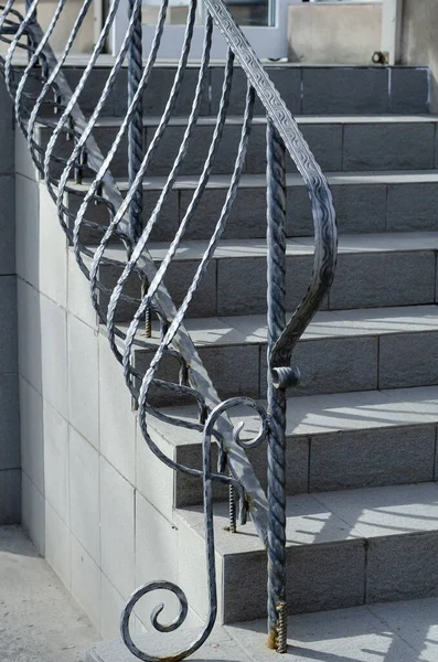 Gray stone staircase with wrought iron railings. Graceful railings enclose the steps covered with ceramic tiles. Entrance to the building. Selective focus.