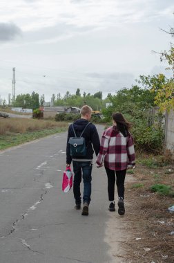 Heteroseksüel bir çift yol boyunca el ele yürüyorlar. Sevilen erkek ve kadın. Aşk, ilişkiler. Bulutlu bir sonbahar günü. Arka plan.