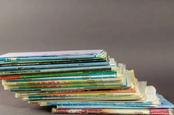 Stack of old school exercise books on a gray background. Random thin notebooks are stacked on top of each other. Close-up. Selective focus.