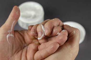 El masajı kozmetik kremi. Orta yaşlı bir adam ellerinin derisini yüzer. Kremalı ve arka planda kapağı olan bir kap..