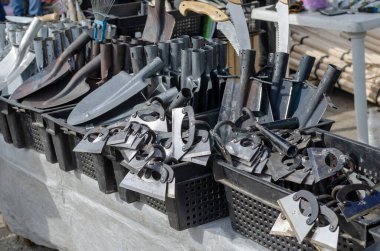 İçinde yeni metal bahçe aletleri olan bir tezgah. Bahçe kürekleri, çapalar ve siyah plastik kutulardaki testereler. Bahar Çiftçi Fuarı. Bahçe ve mahsul üretimi.