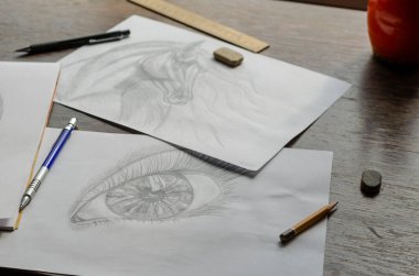 Kahverengi ahşap bir masanın üzerinde duran bir kalem tarafından yapılan çizimler. At portresi ve beyaz kağıda insan gözü çizilmiş. Kalemler, silgi ve cetvel. Sanat, hobi ve eğlence. Sanatçı yeteneği. Kapalı.