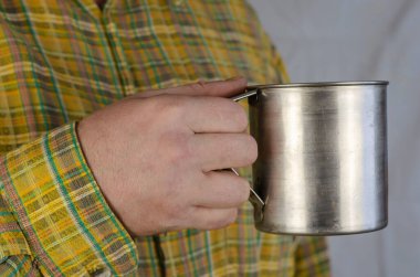 Sarı kareli gömlekli yetişkin bir adamın elinde metal bir kupa var. Orta yaşlı bir adam, Kafkasyalı, içeride. Yakın çekim, seçici odaklanma.