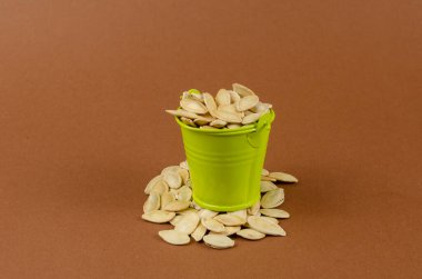 Kahverengi arka planda küçük kova ve kabak tohumları. Kavrulmuş tohumlarla dolu yeşil bir vermut. Atıştırmalık hazır. Yakın çekim, seçici odaklanma.