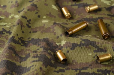 Kamuflaj bezinde rastgele birkaç kovan. Bir grup tabanca ve boş kovan askeri üniformaların üzerinde yatıyor. Ordu teması.