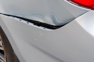 Trafik kazası oldu. Hasarlı arka çamurluğa ve gri bir sedanın tamponuna yakından bakın. Tampon parçaları kopmuş ve araba gövdesinde göçükler var. Aracın sol arka tarafında. Otomatik Sigorta