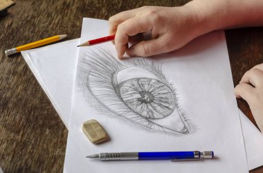 Orta yaşlı bir kadın beyaz kağıda kalem çizer. Yetişkin bir kadın ahşap bir masaya oturur ve bir insan gözü çizer. Sanat, hobi ve eğlence. Sanatçı yeteneği. Kapalı.