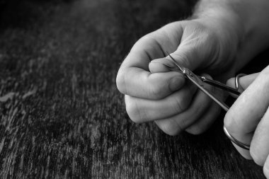 Yetişkin bir adam manikür makası ile el tırnaklarını kesiyor. Onun elleri kahverengi bir ahşap masanın üzerinde dinleniyor. Yakın plan. Seçici odaklanma. Tek Renkli