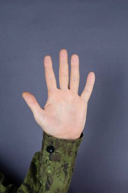 El kamuflajı, parmaklarının gri arka planda olduğunu gösteriyor. Avuç içini dikey aç. Ordudaki beş sayısının ataması. Ordu jest dili.