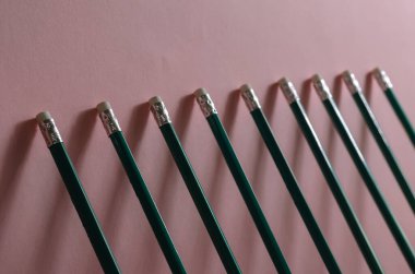 Tahta kalemlerle geometrik minimalist kompozisyon. Aynı yeşil kalemler pembe bir duvara yaslanıyor. Yakın plan. Seçici odak.