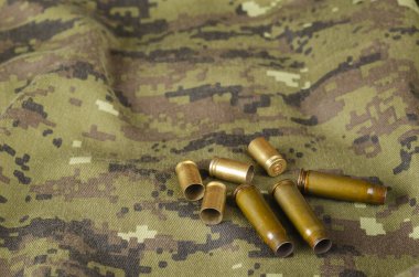 Kamuflaj bezinde rastgele birkaç kovan. Bir grup tabanca ve boş kovan askeri üniformaların üzerinde yatıyor. Ordu teması.