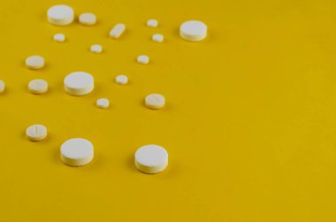 Sarı arka planda rastgele beyaz ilaç içeren minimalist bir kompozisyon. Bir açıdan yan görüş. Büyük plan, seçici odaklanma. Boşluğu kopyala