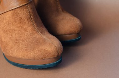 Kahverengi arka planda ince topuklu kahverengi süet kadın botları. Doğal malzemeden yapılmış şık kadın ayakkabıları..