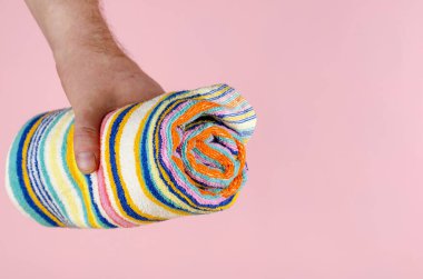 Pembe arka planda çizgili havlu ve El. Elinde çok renkli bir havlu tutan adam. Yan görüş. Seçici Odaklanma.