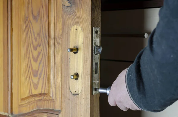 A man removes the old door lock. Hands with a screwdriver unscrew the mounting screws of the mortise lock of a wooden interior door. Services to repair or replace furniture fittings. Indoors