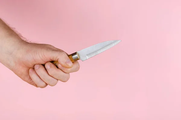 ピンクの背景に小さなナイフと手 男は木製のハンドルを持つ金属製のキッチンナイフを持っています サイドビュー スペースのコピー — ストック写真