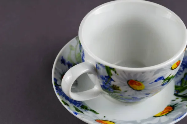 White cup with painted flowers on a gray background. Ceramic Mug cup and saucer for tea or coffee brightly decorated in blue and yellow colours. White daisies on the dishes.