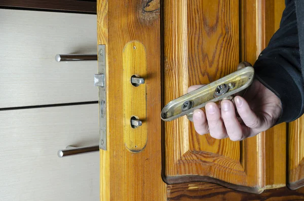 A man removes an old mortise lock on a wooden interior door. The hand holds the overlay bar of the lock with the door handle. Furniture hardware repair or replacement services. Indoors.