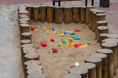 Dikey yuvarlak kütüklerle çevrili boş çocuk kum havuzu. Bahar yağmurundan sonra renkli plastik oyuncaklarla ıslak kum havuzu. Şehir parkındaki çocuklar için oyun alanı.