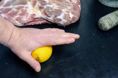 Ev yapımı Capicola (coppa). Kurutulmuş domuz filetosu adım adım tarifi. Bir el olgun bir limonu kabuğuyla masaya bastırır. Bir adam et marine etmek için limonun suyunu sıkar..