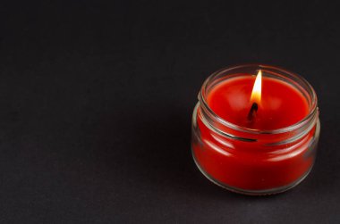 Siyah arka planda cam bir kavanozda yanan kırmızı bir mum. Yarı karanlıkta bir mum alevi gibi. Yan görüş. Boşluğu kopyala.