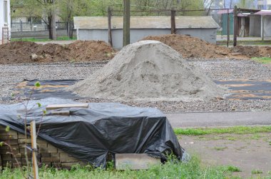 Tuğlalar ön planda siyah plastik ambalajla kaplıdır. Arka planda ıslak kum yığını. İnşaat işleri, peyzaj işleri..
