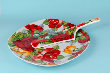 Mavi arka planda spatulası olan seramik kek tabağı. Yuvarlak köşeli kare tabaklar kırmızı güllerle süslenmiş..