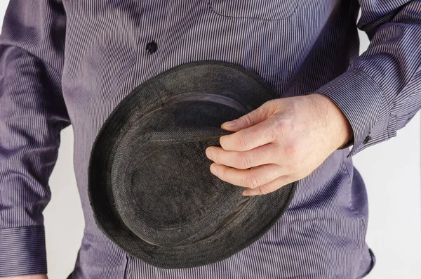 Middle section of man in blue shirt on a white background. Adult male holding a black hat with small brim in his hand. Selective Focus