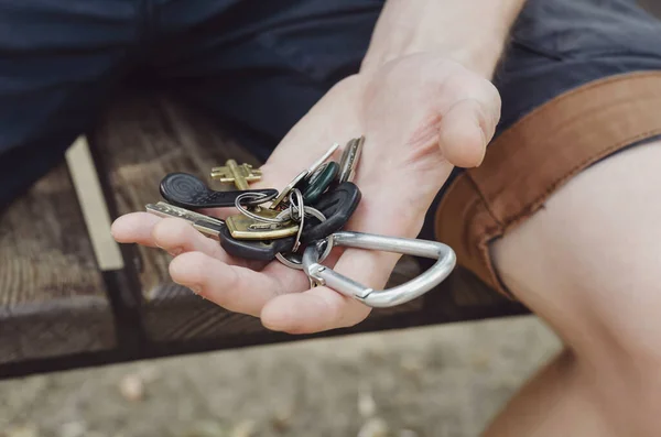 一个年轻的成年人手里拿着一把钥匙 一个拿着钥匙的男人坐在公园的长椅上 有选择的重点 — 图库照片