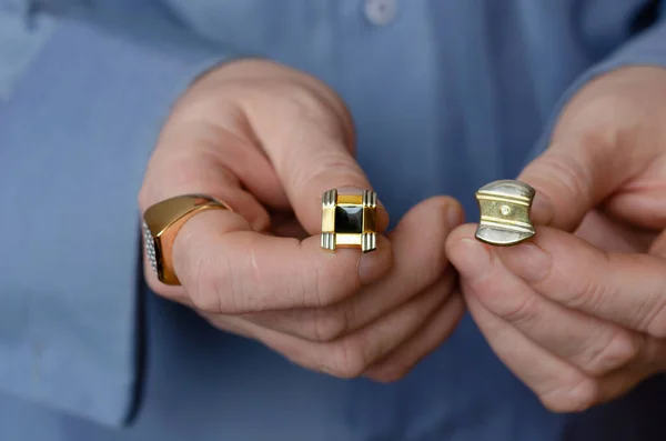 Concept of choice. Close-up of hands holding two different cufflinks. A middle-aged adult man with a gold ring on his index finger showing off his clothing accessories.