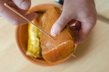 Bir el mutfak masasının üzerine ahşap bir sopayla bir parça domuz filetosu sokuyor. Arka planda marine edilmiş et olan kilden bir tabak. Kurutulmuş domuz eti hazır. Üst görünüm.