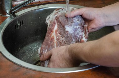 Ev yapımı Capicola (coppa). Kurutulmuş domuz filetosu adım adım tarifi. Adam bir parça domuz etinin tuzunu yıkıyor. Elleri terbiye edilmiş eti akan suyun altında tutuyor. Geleneksel İtalyan mutfağı