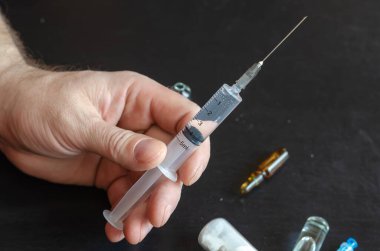 Bir el, üç ampul ve bir şişe beyaz toz. El, ilaç şırıngasını tutuyor. Yakın çekim, seçici odaklanma.