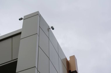 Bej ve Brown binasının köşesindeki güvenlik kamerası sistemi. Bulutlu bir gökyüzüne karşı iki video kamera. Gündüz vakti. Yağmurda çekim. Mimari.