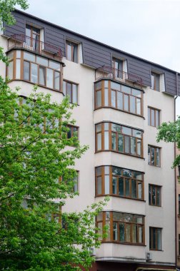 Kahverengi çatılı ve balkonlu bej bir bina. Bulutlu gökyüzüne karşı modern daireler. Gündüz vakti. Yağmurda çekim. Mimari.