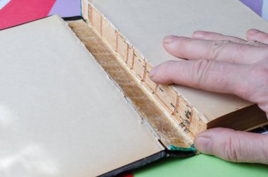 Eski yırtık bir kitap ve yakın plan el çekimi. Yetişkin bir erkeğin sağ eli, açık yaprak kaplı defter üzerinde yatıyor. Kağıt kitap tamiri konsepti. Seçici odak.