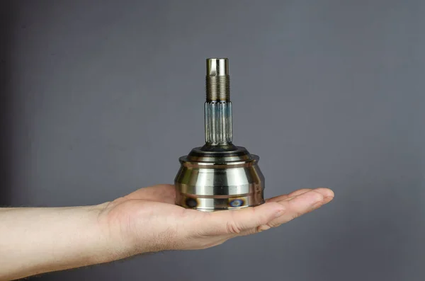 A man demonstrates a Drive shaft joint against a gray background. New Constant velocity joints.  Spare parts, consumables. Side view.