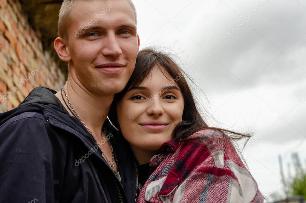 Portrait of a young heterosexual couple standing in an embrace. A young woman with long dark hair and a young man with short hair. Happy lovers are looking at the camera.