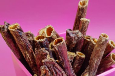Pembe arka planda bir kutu ödül. Yavru köpekler, yetişkin köpekler ve son sınıfların köpekleri için kurutulmuş dişçi malzemeleri. Lezzetli Red Beef Gullet çubukları. Sığır yemek borusu. Hediye paketi.