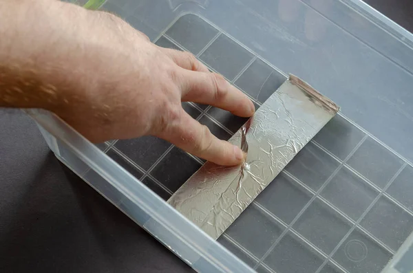 A man seals a crack in a plastic container with aluminum tape. The process of repairing a clear food container.   View from above from an angle. Selective focus.