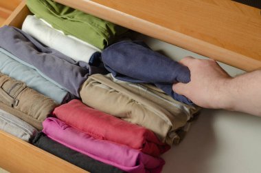 Dikey Japon giysi depolama sistemi kavramı. Konmari metodunu kullanarak şifoniyer rafına istiflenmiş çok renkli gömlekler. Bir adam ev işleriyle meşgul.