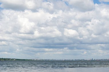 Geniş nehrin üzerindeki bulutlu gökyüzü Güney Böceği. Katı bulutluluk. Arka planda limanlar, tahıl asansörleri ve Nikolaev şehrinin tersanesi var. Muhteşem bir Ukrayna yaz manzarası.