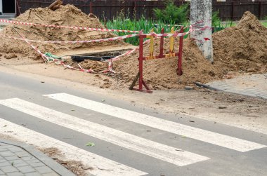 Yaya geçidinin arkasında çukur kazdık. Bariyer bandı ve ahşap bariyerlerle dolu derin bir çukur belediye onarımı ya da inşaat çalışmaları yapılan bir yer. Gündüz.