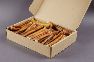 Pet Treats. Cardboard box full of chew sticks. Natural chewy treats for dogs on gray background. 6-inch Bully sticks. Dried bovine penis. Beef pizzle. Angled view from above.