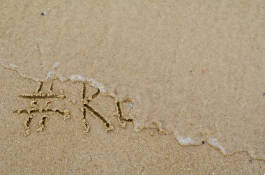 Tatilin Sonu kavramı. Dalga hashtag 'i ve sarı kumda dinlenme kelimesini silip süpürüyor. Islak kumsalda el yazısıyla yazılmış bir kelime. Büyük harflerle. Yukarıdan görüntüle.