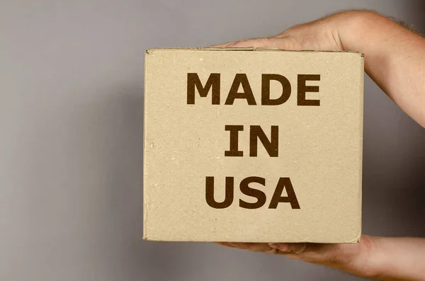 灰色の背景にアメリカ製品の箱 リサイクル材料の正方形のパッケージを持つ男 アメリカで作られた碑文 世界貿易の概念 サイドビュー — ストック写真