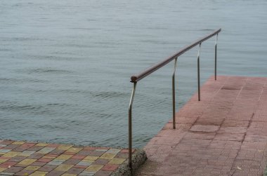 The end of a red stone walk to the sea. The metal fence is on the left. Trampoline to jump to bathe in the sea